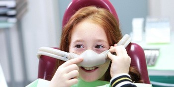 Girl in dental chair touching the nitrous oxide mask over her nose