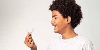 Teenage boy smiling while holding clear aligner