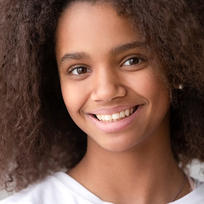 A young girl wearing a white shirt and smiling after visiting a practice that offers pediatric dentistry in Phillipsburg