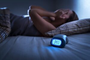 Sleepless person in bed in background with clock in foreground. 