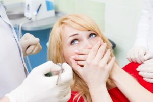 Woman in dentist’s chair covering her mouth with both hands in fear.